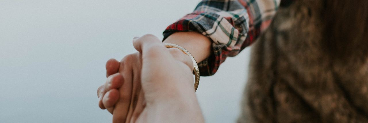 How to Help Someone Get Help for Mental Health When They Don't Want It photo of woman reaching hand back to someone and holding their hand while leading them away