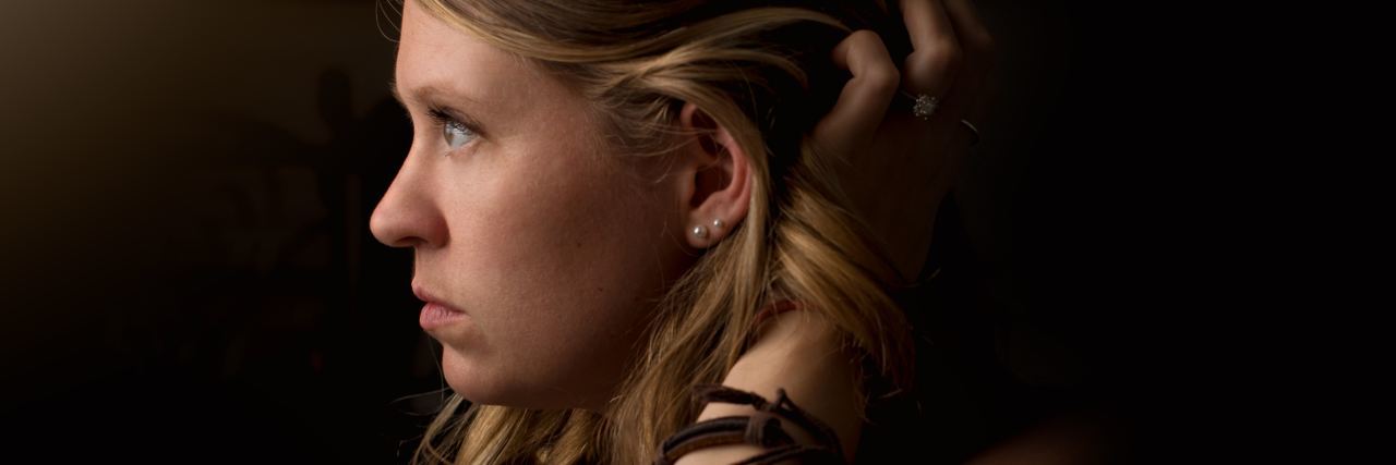 What It's Like to Live With Autism and Anxiety and They Clash photo of young woman in profile view with darkness behind her and her hand in her hair