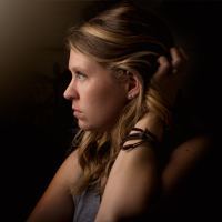 photo of young woman in profile view with darkness behind her and her hand in her hair