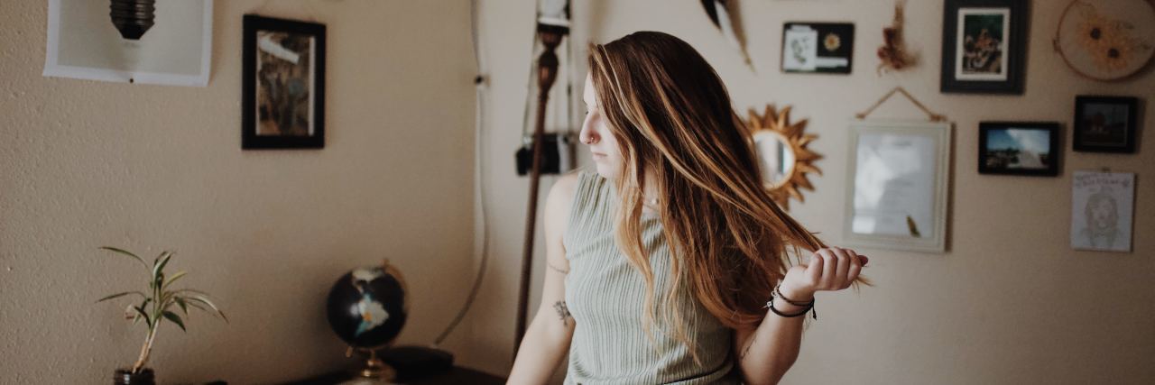 Read This If You're Struggling to Adjust to Life After the Psych Ward Photo of young woman standing in room with one hand on chair and the other playing with her hair. she looks thoughtful or lost.