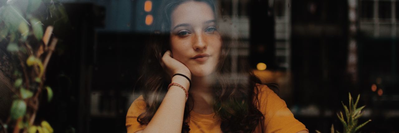 photo of young woman seen through window with head resting on hand