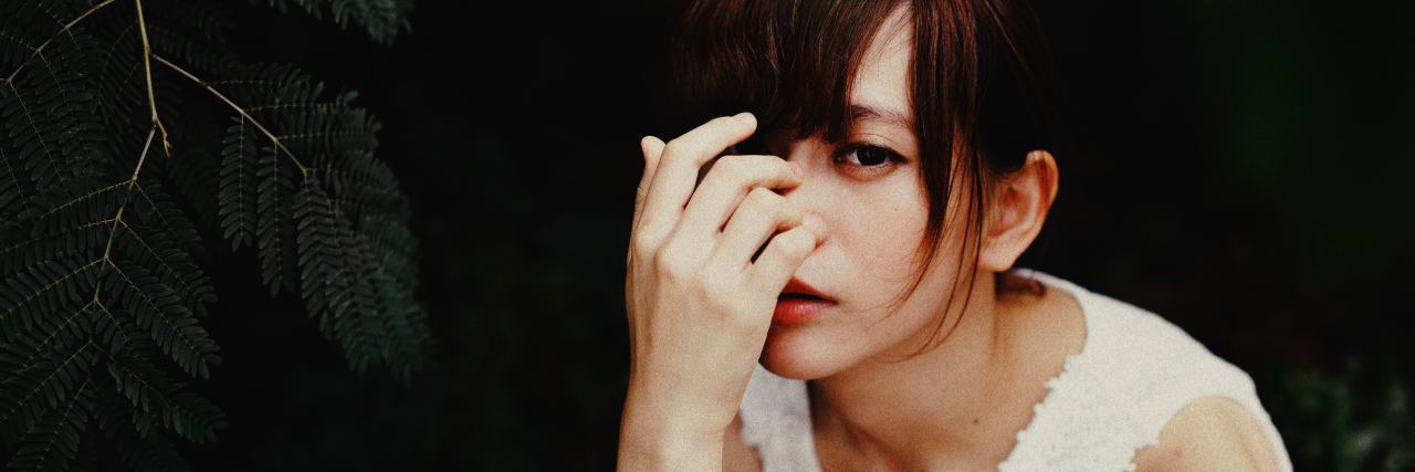 Don't Say Borderline Personality Disorder Is an Excuse photo of young woman covering part of face with her hand, looking sad into camera