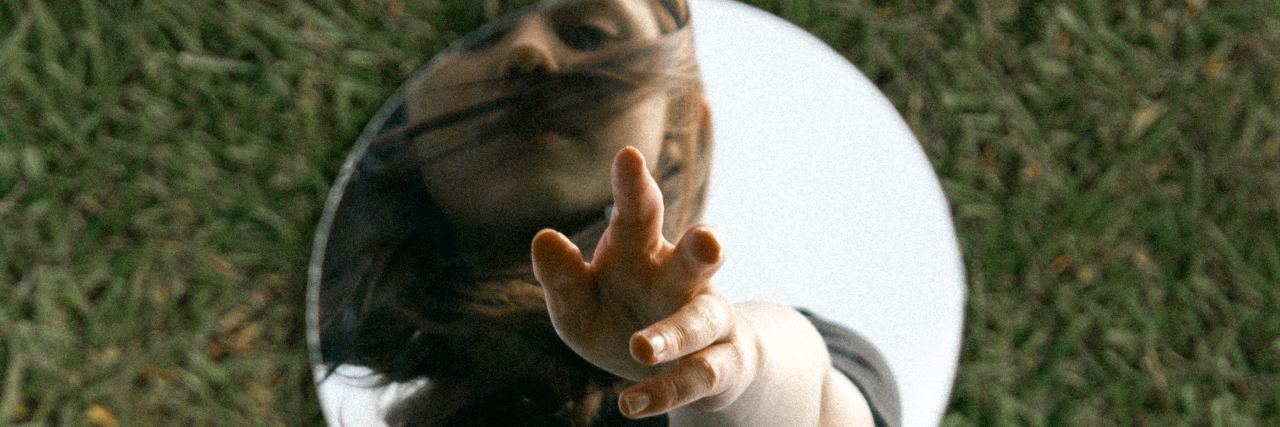 photo of circular mirror on grass with woman reaching into it