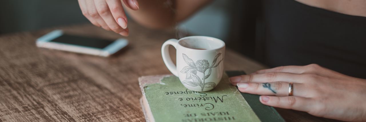 How I'm Productively Dealing With Feelings of Emptiness A woman with a cup of tea and a book, sitting at a table
