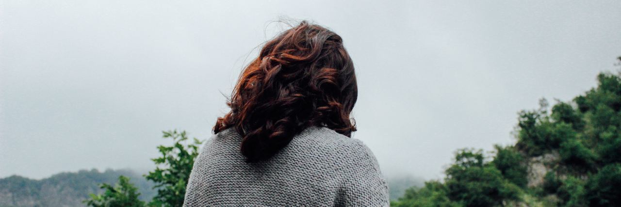 Questioning Your Identity With Chronic Illness the back of a woman, facing trees and skies