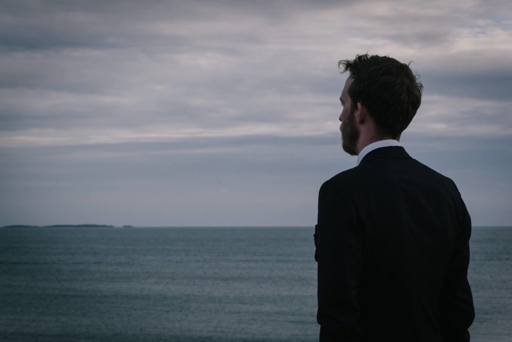 the author wearing a suit and looking out at the sea at dusk