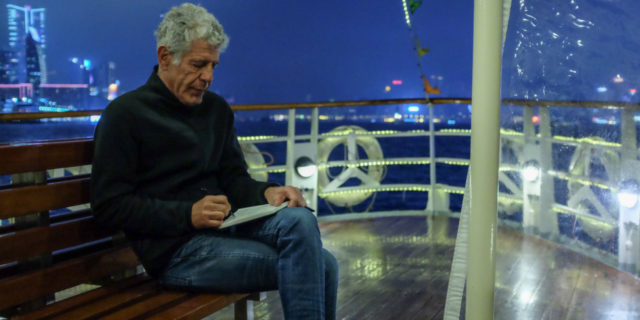 photo of anthony bourdain sitting on a boat, writing