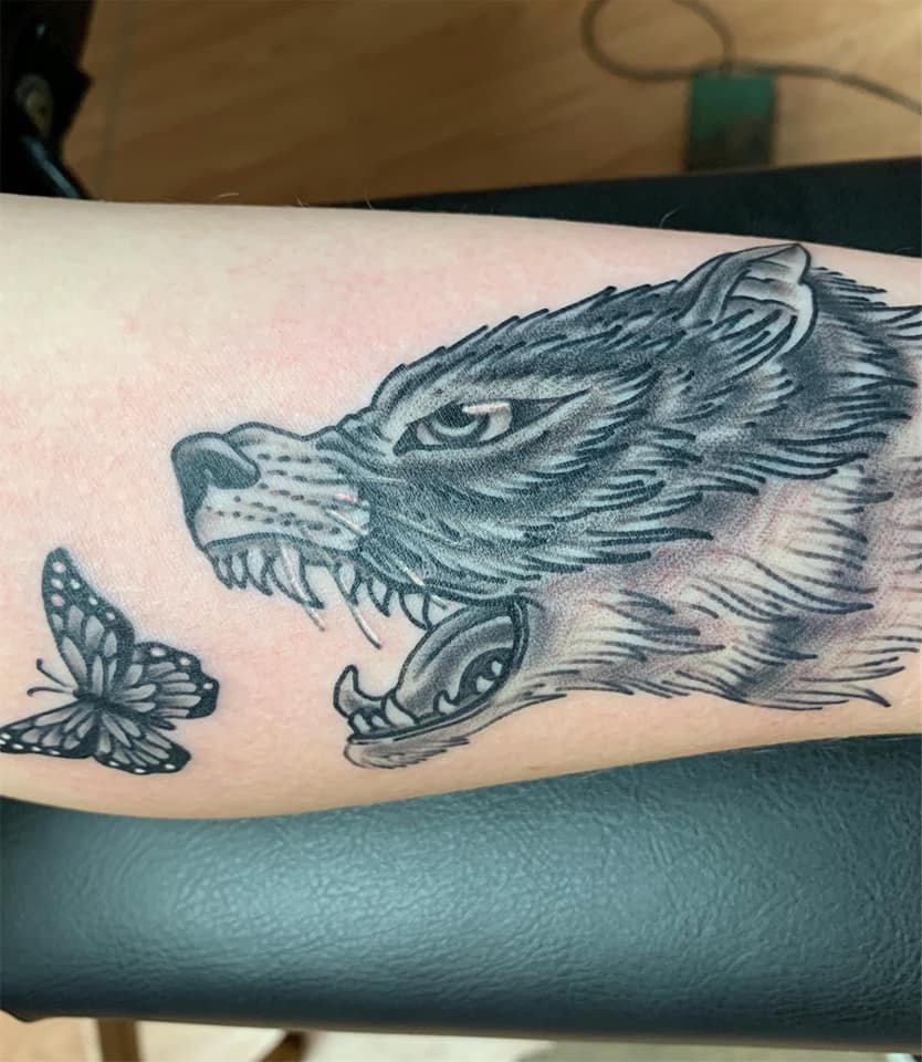 black and white tattoo of a wolf chasing a butterfly with its mouth open. it represents migraine, fibromyalgia and lupus