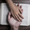 Two hands holding each other on a bible