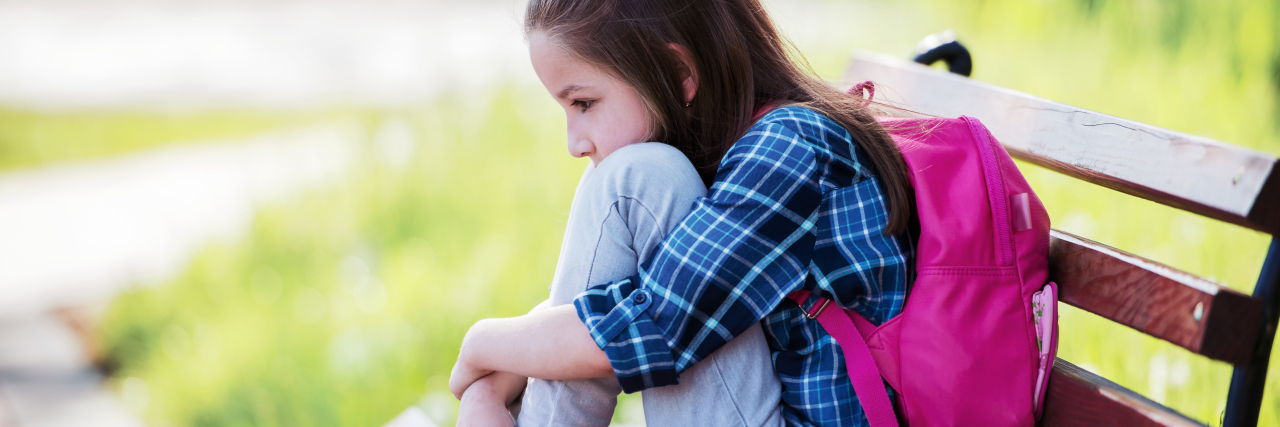 Why Society Is Failing Autistic Children Sad girl sitting on park bench outside school.