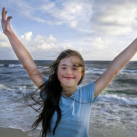 Girl with Down syndrome smiling with arms spread wide and ocean in the background