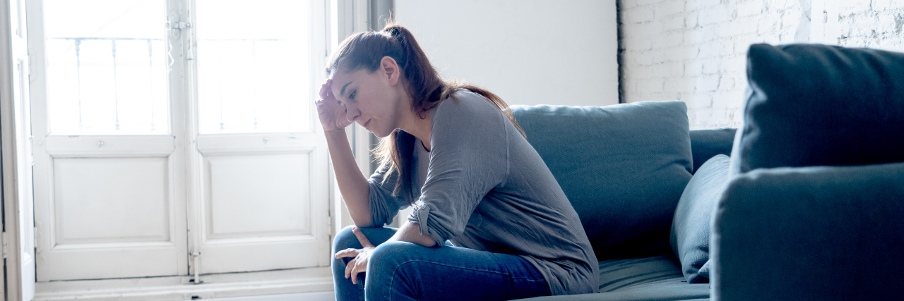 Trying to Have a Daily Routine While Living With Chronic Illness woman sitting on couch by the window, looking upset and frustrated