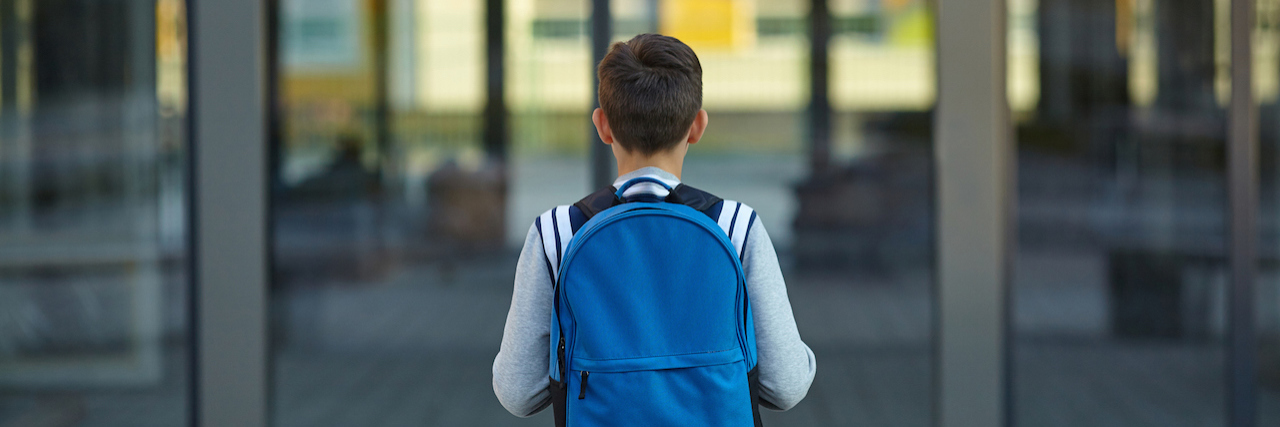 A young boy wearing a backpack looking at the front door of a school