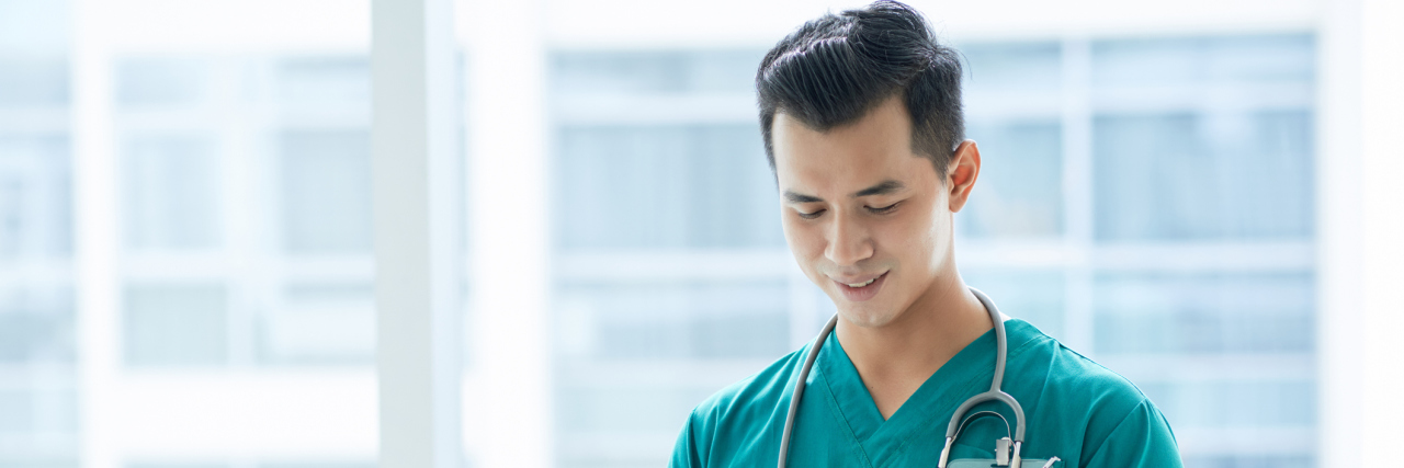 The Advice I’d Give Chronic Illness Patients After Shadowing a Gastroenterologist A medical professional stands looking down at a cellphone.