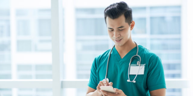 A medical professional stands looking down at a cellphone.