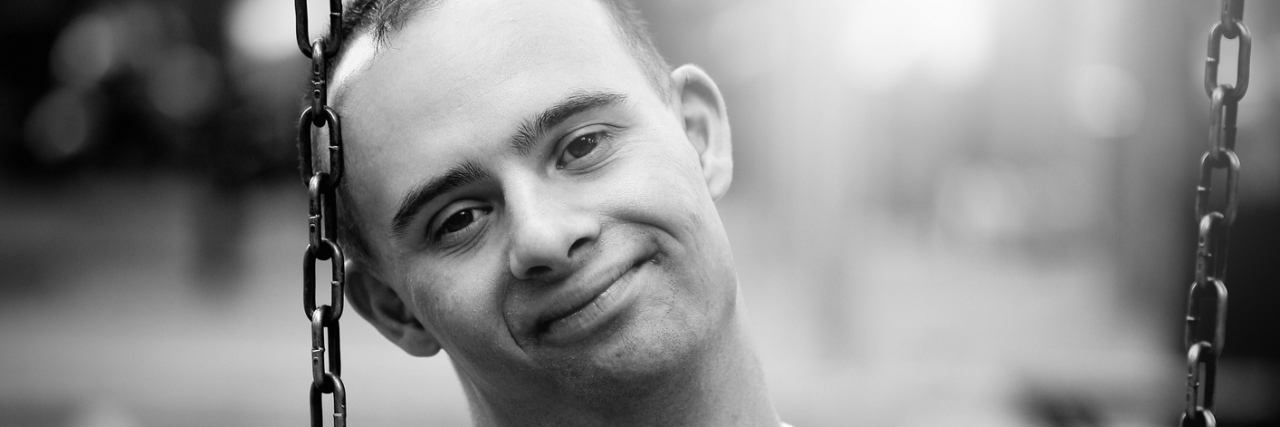 The One Stereotype About Down Syndrome I'm Tired of Hearing Black and white image of man with Down syndrome sitting on swing and slightly smiling