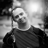 Black and white image of man with Down syndrome sitting on swing and slightly smiling