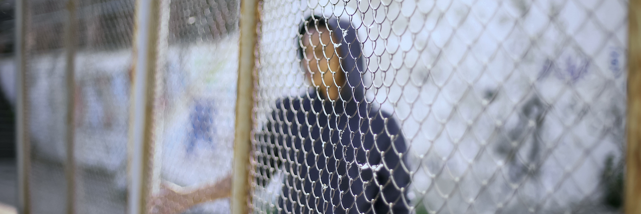 The Traumatic Impact of Housing Children in Detention Centers A young man behind a fence
