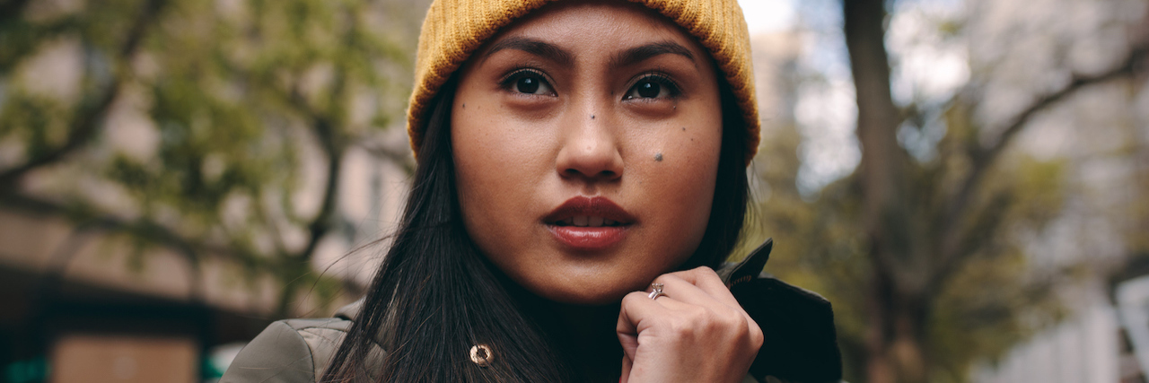 Can't Talk to My Filipino Parents About My Anxiety A Filipino woman standing on the street, wearing a winter coat and a hat