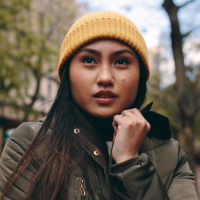 A Filipino woman standing on the street, wearing a winter coat and a hat