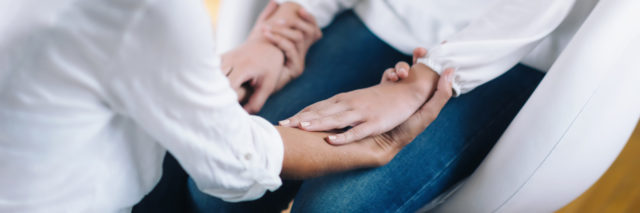 a woman is sitting with her therapist holding hands