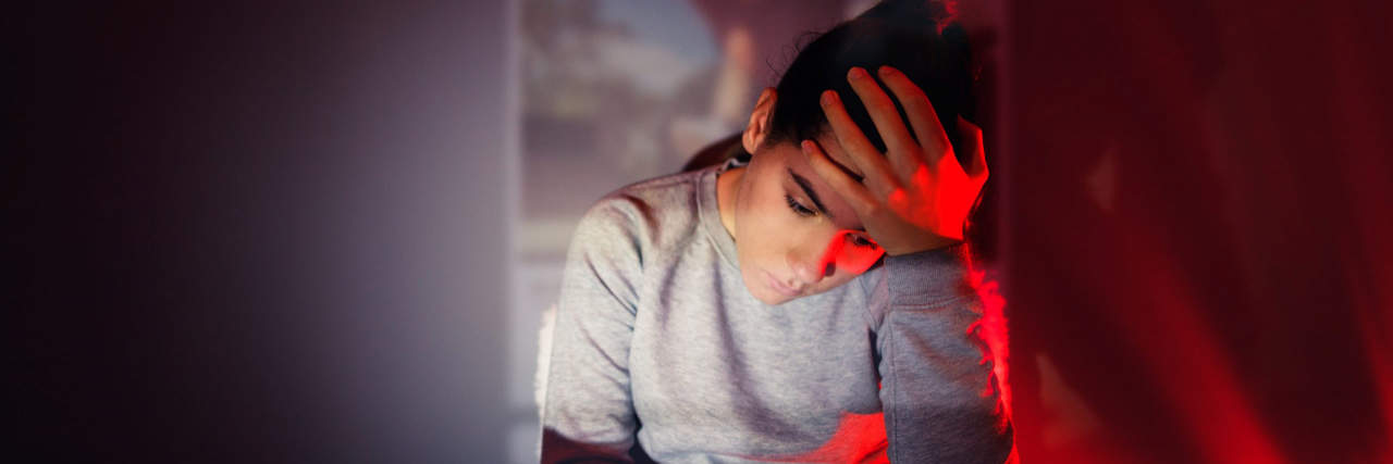 A Letter to Someone Just Diagnosed With a Chronic Illness a girl with her hand on her head looking concerned at her phone in dark artful lighting