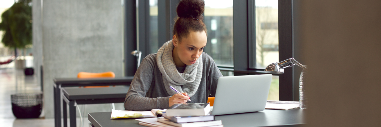 10 Ways to Prepare Your Autistic Child for College Young female student working on a laptop with books nearby.