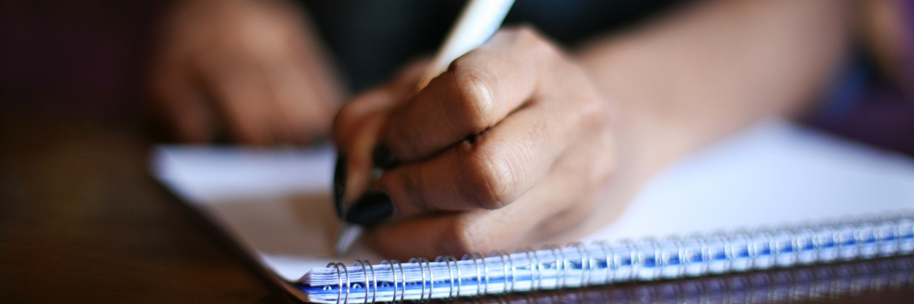 What It's Like to Live With Myasthenia Gravis for the First Year woman's hand with a pen, writing in a notebook