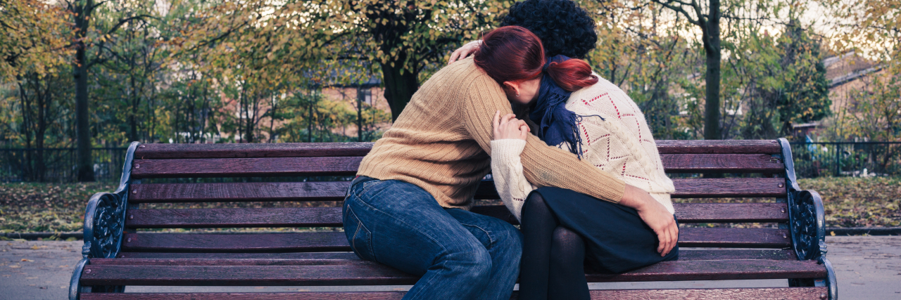A couple is embracing while sitting on a park bench