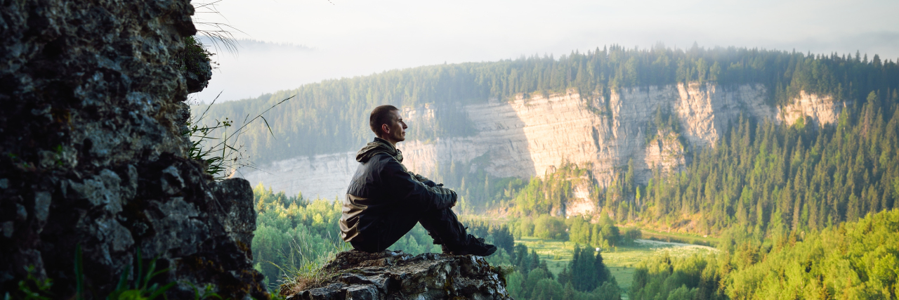 Forgiving My Hard Days With Stuttering Man sitting on top of a mountain.