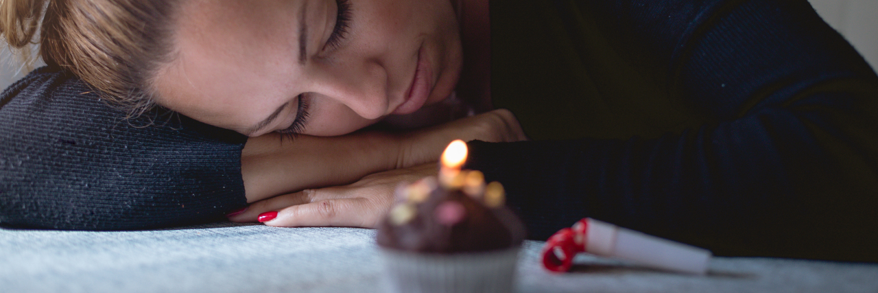 photo of woman lying her head down on hands looking at cupcake with birthday candle