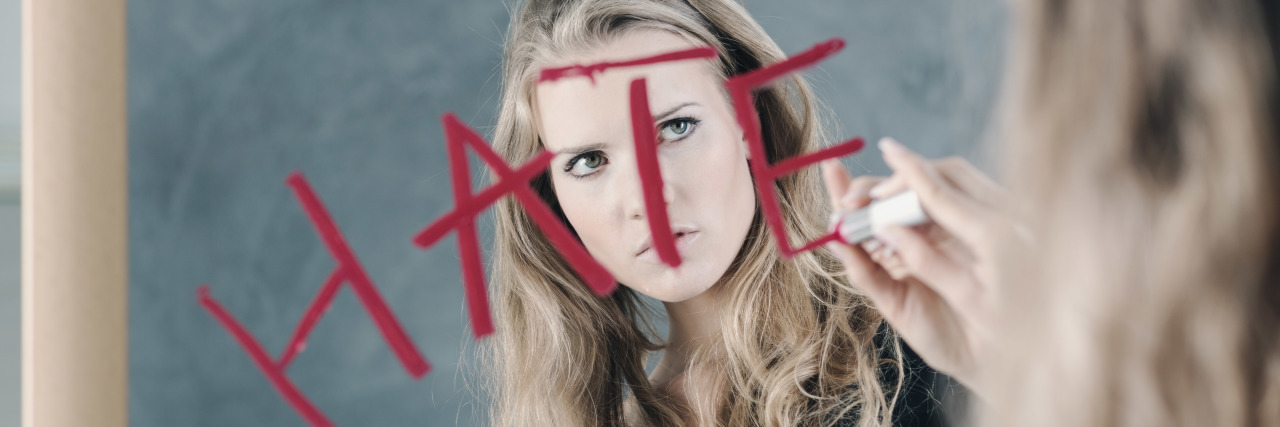 When Borderline Makes You Your Own Bully a woman is writing the word "hate" on a mirror