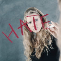 a woman is writing the word "hate" on a mirror