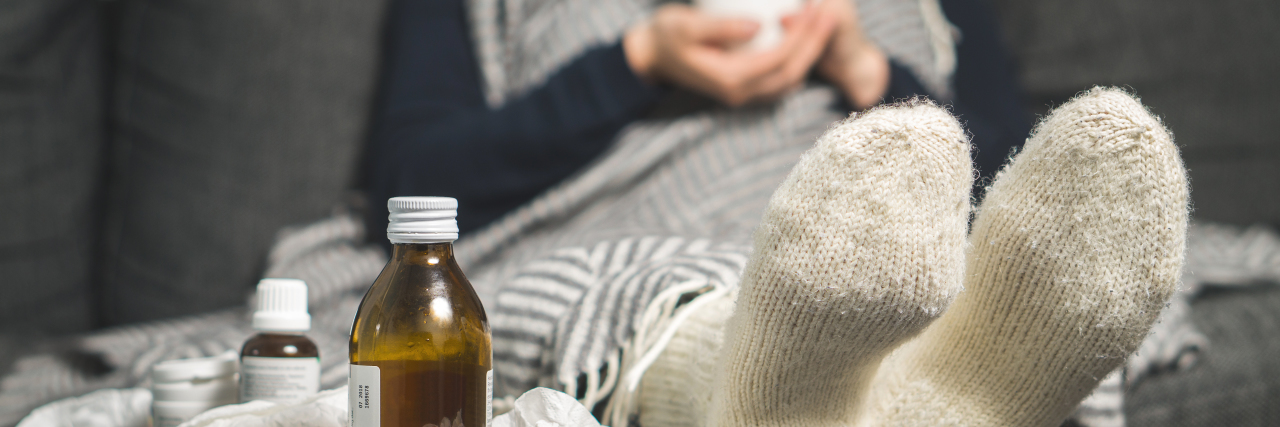 The Problem With Getting Sick While Chronically Ill Woman sick on the couch with tissues.