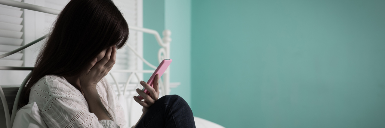 Why Am I Angry Crying? woman sitting on bed crying and looking at phone