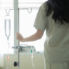 photo of woman standing at window holding IV drip pole