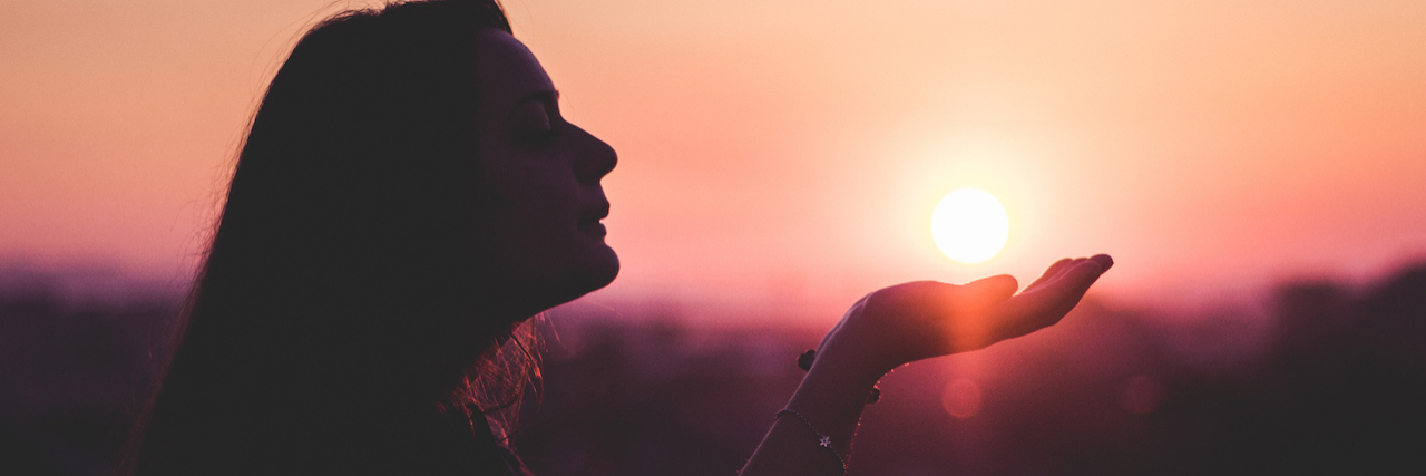 Why Anorexia Is Like Being in an Abusive Relationship A woman in shadows holding her hands up to the sun, as if to top it with her hands. the sky is colored like a sunset.