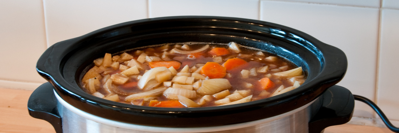 Slow cooker with stew and a wooden spoon