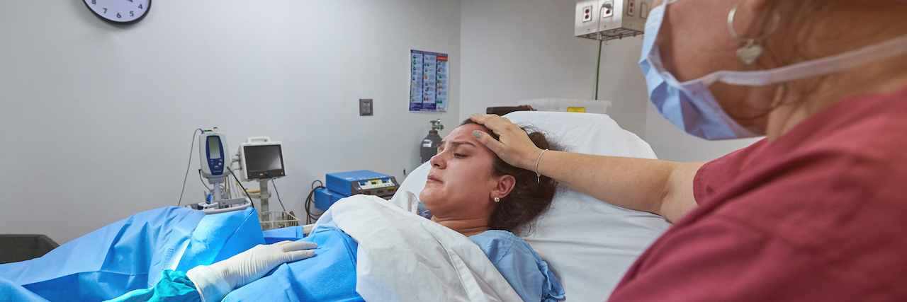 I Have PTSD After a Traumatic Birth Due to Medical Negligence A woman in the delivery room, a nurse touches her head