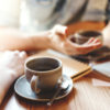 Friends talking at cafe table, focus on coffee cups and hands