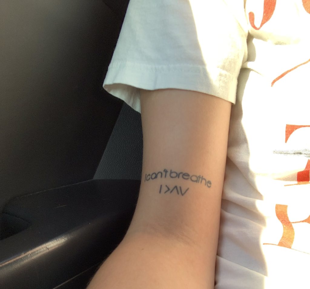 black tattoo on woman's arm that says 'I can't breathe.' underneath it says 'I am greater than my highs and lows' using symbols