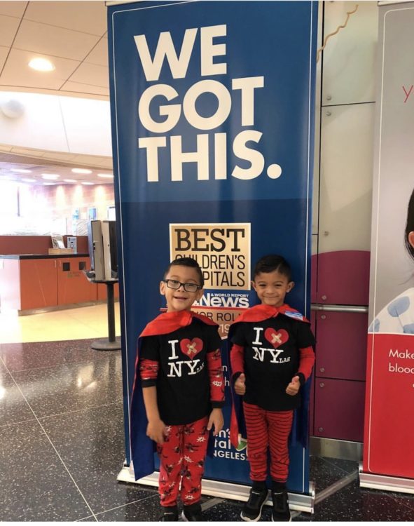 A set of twin boys wearing super hero capes and smiling for the camera.