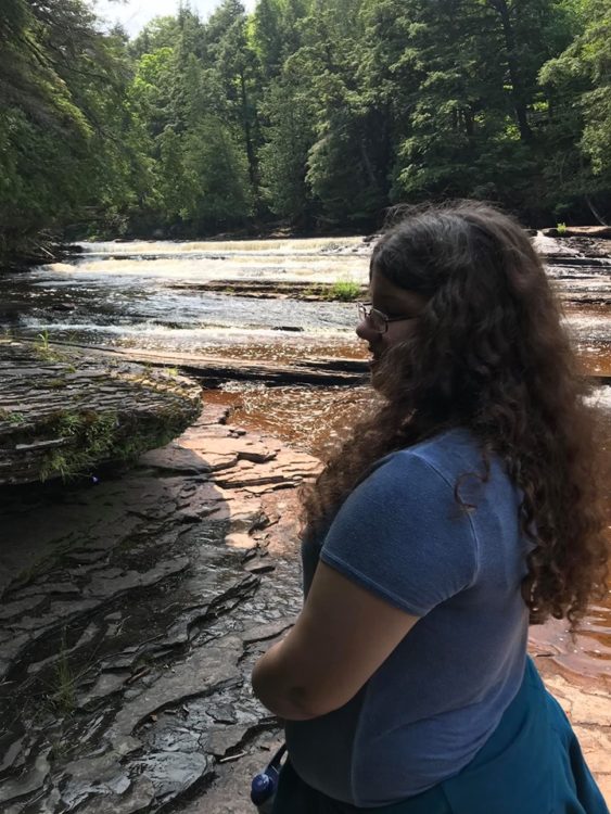 naomi, standing by a creek and the woods