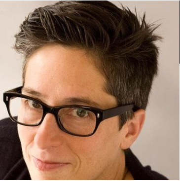 Alison Bechdel, cartoonist. She has short brown hair and is wearing glasses and a black shirt.