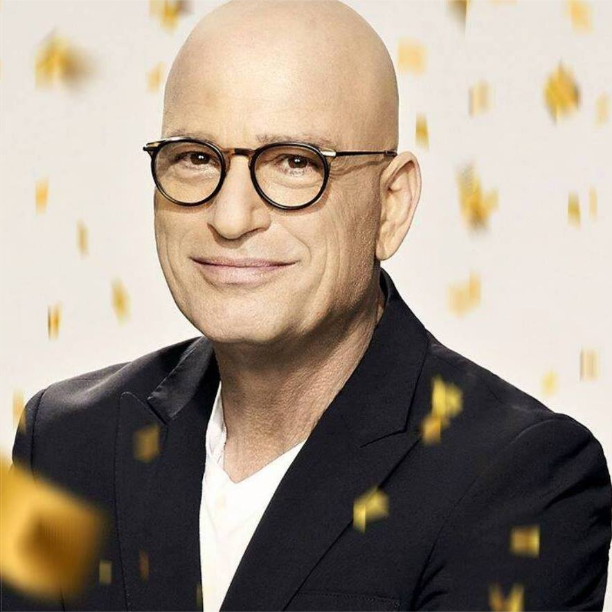 Howie Mandel, Canadian actor, poses as a stream of confetti falls down. He is bald and is wearing glasses. He is wearing a black coat and white T-shirt.