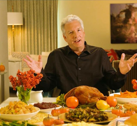 Marc Summers, apresentador de televisão, senta-se antes de um grande banquete. Ele tem o cabelo branco. Ele está vestindo uma camisa preta.