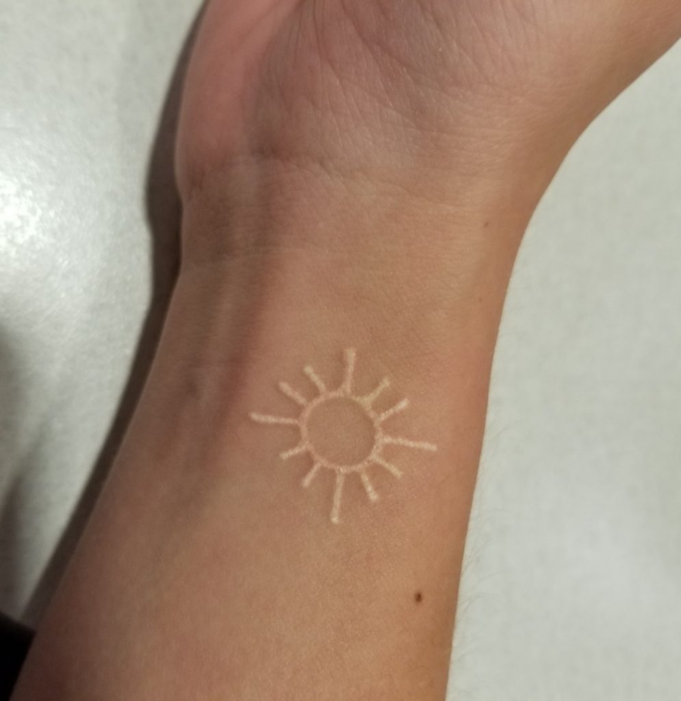 small white sun tattoo on woman's wrist