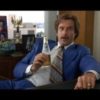 Ron Burgundy from Anchorman, sitting at his desk and holding a beer