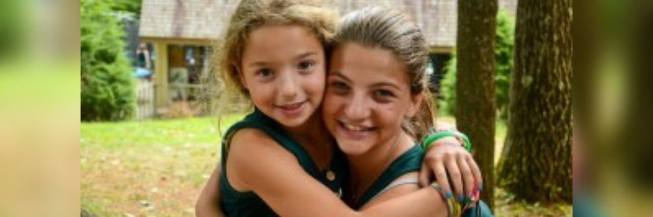 The author with her arms around her little sister. They're both wearing green tank topics, and standing outside