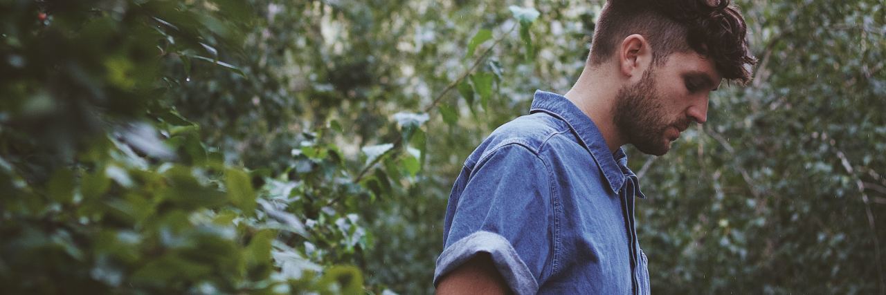 Read This If You've Been Treated Badly Because of Your Chronic Illness photo of young man in profile view looking down with trees or leaves behind him